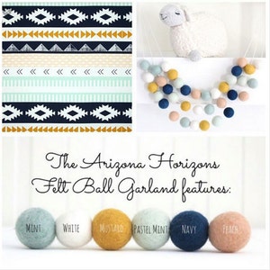 May include: A felt ball garland with a variety of colors, including mint, white, mustard, pastel mint, navy, and peach. The garland is hanging from a white ceiling and is decorated with a white sheep. The text "The Arizona Horizons Felt Ball Garland features:" is written below the garland.