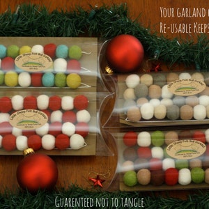 May include: Four clear plastic boxes with felt ball garlands inside. The garlands are red, white, green, and brown. The boxes are on a wooden surface with green garland around the edges. The text "Your garland comes in a re-usable keepsake giftbox" is at the top of the image. The text "Guaranteed not to tangle" is at the bottom of the image.