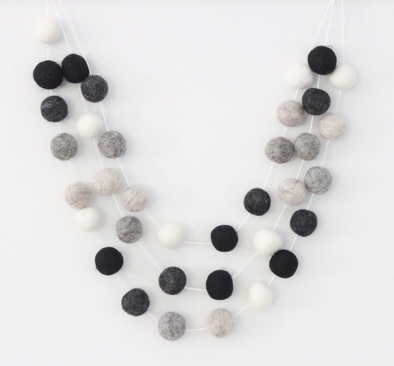 Peut inclure: Une guirlande de boules en feutre noires, blanches et grises. Les boules sont enfil&eacute;es sur un fil blanc et dispos&eacute;es en cascade.