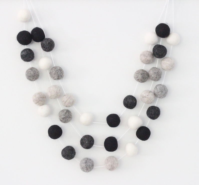 May include: A garland of felt balls in black, white, and gray. The balls are strung on white thread and are arranged in a cascading pattern.