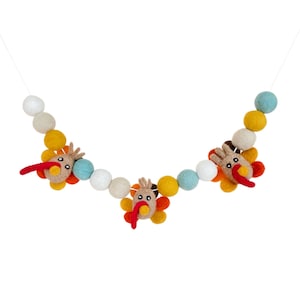 May include: A garland with felt balls in white, yellow, blue and orange. The garland features three felt turkey ornaments with brown bodies, orange and yellow feathers, red beaks and black eyes.
