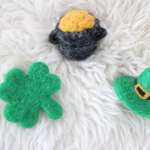 May include: A felt shamrock, a felt pot of gold, and a felt leprechaun hat. These are all green and yellow felt decorations.