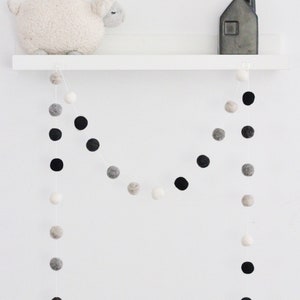 May include: A white shelf with a white stuffed sheep, a black and white felt ball garland, and a black vase with a bouquet of black and white felt balls.