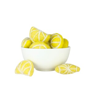 May include: A white bowl filled with yellow felt lemon slices. The bowl is sitting on a white surface.