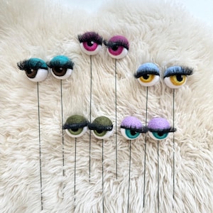 Peut inclure: Neuf paires d'yeux en feutre avec des cils sur des tiges de fil. Les yeux sont de diff&eacute;rentes couleurs, notamment le vert, le bleu, le violet, le rose, le marron et le jaune.