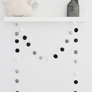 Peut inclure: Une &eacute;tag&egrave;re blanche avec un mouton en peluche blanc, une guirlande de boules de feutre noires et blanches et un vase noir avec un bouquet de boules de feutre noires et blanches.