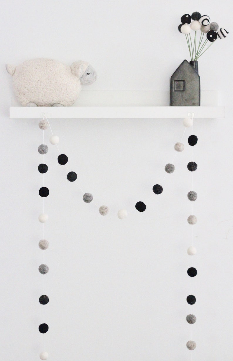 Peut inclure: Une &eacute;tag&egrave;re blanche avec un mouton en peluche blanc, une guirlande de boules de feutre noires et blanches et un vase noir avec un bouquet de boules de feutre noires et blanches.