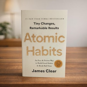 May include: A hardcover book titled "Atomic Habits" by James Clear. The book has a cream-colored cover with the title in large, gold-colored letters. The text reads "Tiny Changes, Remarkable Results" and "An Easy & Proven Way to Build Good Habits & Break Bad Ones."