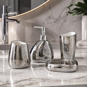 May include: A four-piece bathroom accessory set featuring a metallic silver finish with a reflective, water-spotted texture. The set includes a soap dispenser with a pump, a toothbrush holder, a tumbler, and a soap dish, all with white interiors.