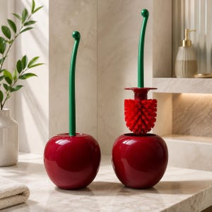 Könnte beinhalten: Zwei kirschförmige Toilettenbürsten-Sets mit glänzend roten, kugelförmigen Behältern und langen, schlanken grünen Griffen. Eine Bürste steckt vollständig im Behälter, während die andere angehoben ist und einen runden, rot beborsteten Bürstenkopf zeigt.