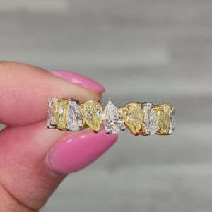 May include: A band ring featuring a series of alternating pear-cut yellow and clear white stones set in a metallic frame. The stones are arranged in a continuous row, showcasing a mix of vibrant yellow and colorless faceted gems in a teardrop shape.