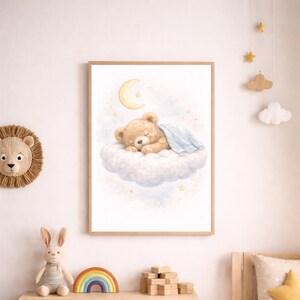 Op de afbeelding: Een ingelijste print met een slapende teddybeer op een wolk, onder een maan en sterren. Het kunstwerk heeft een zachte aquarel stijl met een lichtblauwe deken. De print zit in een houten lijst, geschikt voor een kinderkamer.