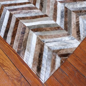 a close-up view of a wooden floor with a rug or carpet laid on it. The rug has a geometric pattern with a mix of brown, gray, and white colors, creating a visually appealing design.
