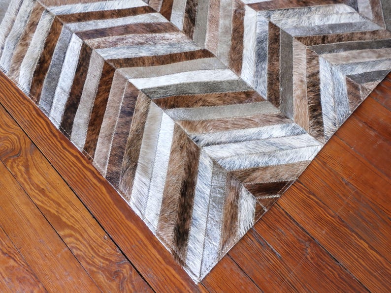 a close-up view of a wooden floor with a rug or carpet laid on it. The rug has a geometric pattern with a mix of brown, gray, and white colors, creating a visually appealing design.