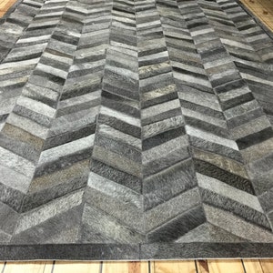 May include: A gray and white chevron patterned rug made from cowhide. The rug is made up of many small pieces of leather sewn together.