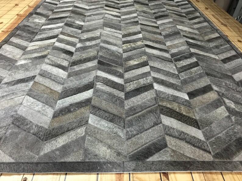 May include: A gray and white chevron patterned rug made from cowhide. The rug is made up of many small pieces of leather sewn together.