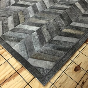 May include: A gray and white cowhide rug with a chevron pattern. The rug has a dark gray border.