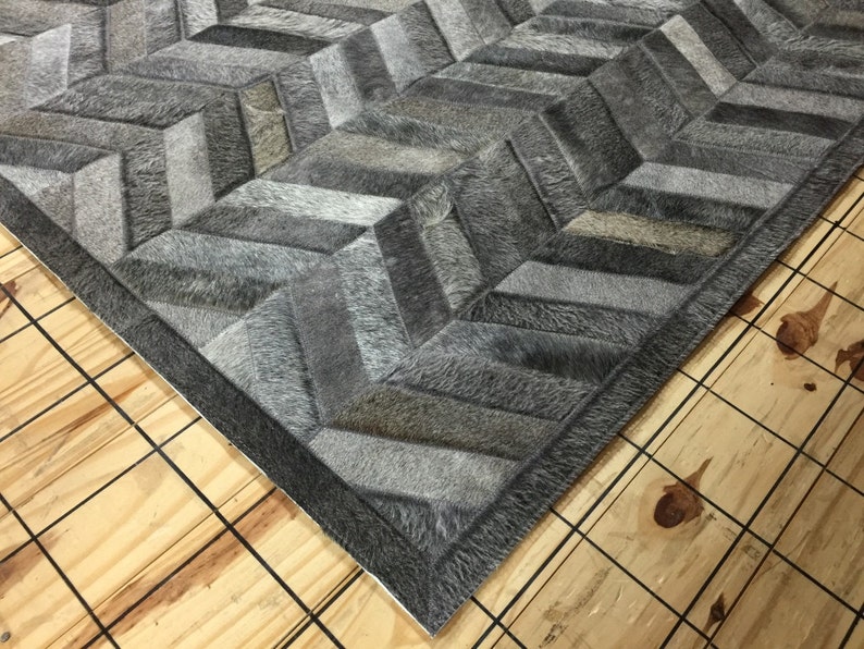 May include: A gray and white cowhide rug with a chevron pattern. The rug has a dark gray border.