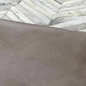 a close-up view of a textured fabric, possibly a rug or a piece of clothing, with a geometric pattern in the background.