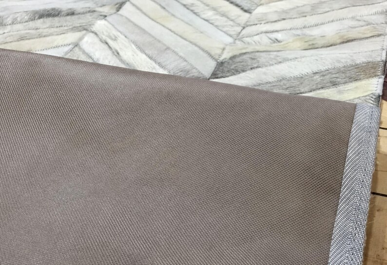 a close-up view of a textured fabric, possibly a rug or a piece of clothing, with a geometric pattern in the background.