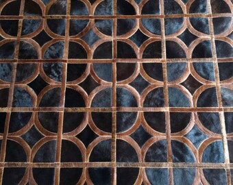 May include: A rug made of stitched cowhide panels featuring a repeating geometric pattern. The design consists of dark black circular shapes framed by light brown leather strips, creating a grid of circles and diamond-shaped negative spaces.