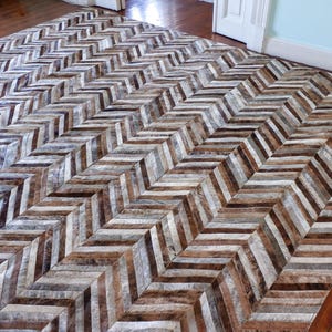 a large, chevron-patterned rug with a mix of brown and gray tones, placed on a wooden floor.