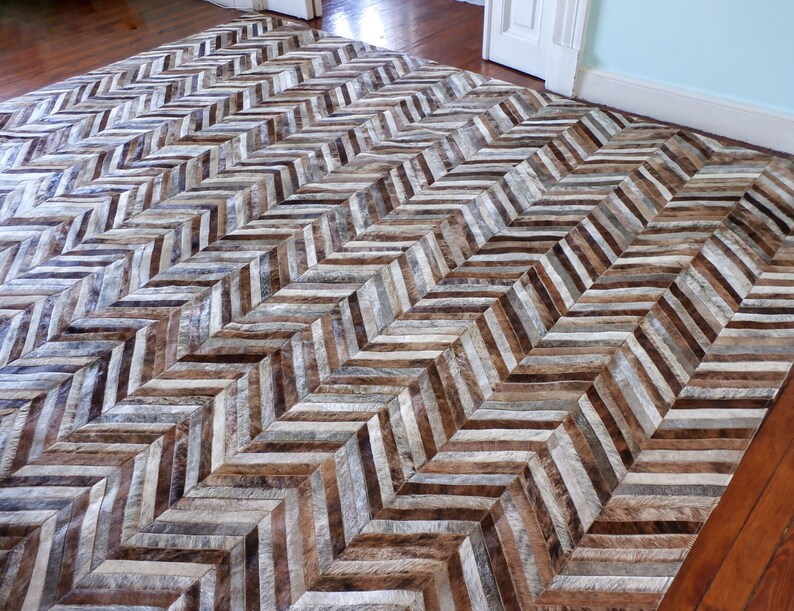 a large, chevron-patterned rug with a mix of brown and gray tones, placed on a wooden floor.