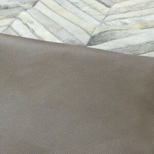 May include: Close-up of the underside of a light gray and white cowhide rug. The rug has a brown fabric backing with a gray stitched border.