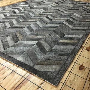 May include: A gray and white chevron patterned rug made from cowhide. The rug has a dark gray border.