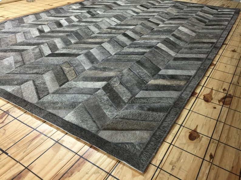 May include: A gray and white chevron patterned rug made from cowhide. The rug has a dark gray border.