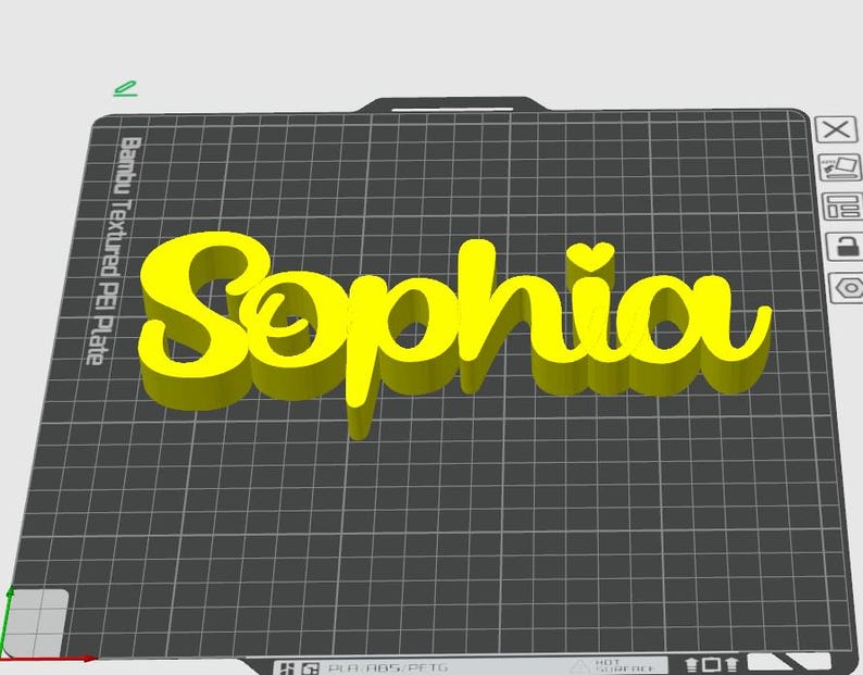 May include: A 3D-printed yellow name, "Sophia", with a heart above the "i". The name is displayed on a black grid surface, with the text "Bambu Textured PEI Plate" visible in the corner. The name is in a cursive font.