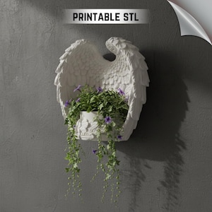 Könnte beinhalten: Weißer Wandtopf mit Engelsflügeln und einem kleinen weißen Topf, der mit grünen Pflanzen und lila Blumen gefüllt ist. Der Pflanztopf hat ein detailliertes Federdesign und der Text "PRINTABLE STL" steht oben.
