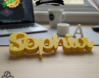 Puede incluir: Un nombre amarillo impreso en 3D, "Sophia", en fuente cursiva, se encuentra sobre una superficie de madera. La imagen incluye un portátil, una taza y el texto "GET CUSTOM NAME". El producto está etiquetado como "BEST CHOICE" y "DIGITAL Download".