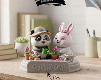 Puede incluir: Una figura decorativa con un panda y un conejito sonriendo. El panda lleva un sombrero y sostiene una regadera, mientras que el conejito tiene un lazo rosa. La base tiene el texto "Candy & ASH" y las palabras "GET CUSTOM NAME".