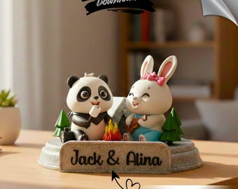 Puede incluir: Figura decorativa con un panda y un conejo acampando. El panda es blanco y negro, y el conejo es blanco con un lazo rosa. Un letrero dice "Jack & Alina". La figura incluye una fogata y pequeños árboles verdes.