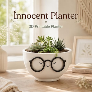 May include: A white ceramic planter featuring a raised black graphic of round glasses and a smiling face. The planter contains various green succulents and is labeled with the text Innocent Planter 3D Printable Planter above it.