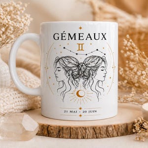 Peut inclure: Mug en céramique blanche avec un design du signe astrologique Gémeaux. Il présente une illustration noire et dorée de deux profils de femmes, le symbole des Gémeaux et le texte "GÉMEAUX". Les dates "21 MAI - 20 JUIN" sont également imprimées.