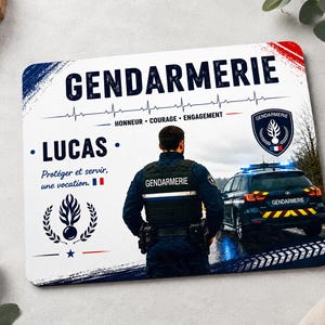 Peut inclure: Un tapis de souris rectangulaire avec le mot "GENDARMERIE" en gros caractères. Le design comprend une ligne de battement de cœur, le nom "LUCAS" et la phrase "Protéger et servir, une vocation." Un policier se tient devant une voiture de police.