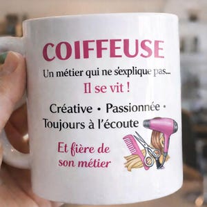 Könnte beinhalten: Weißer Keramikbecher mit dem Wort "COIFFEUSE" in Rosa, französischem Text und einer Grafik eines Haartrockners, einer Schere und eines Kamms. Der Becher wird von einer Hand gehalten.