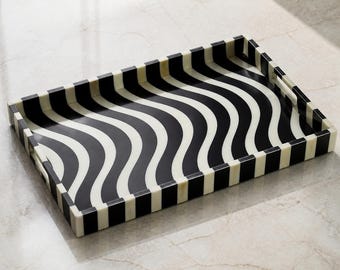 Peut inclure: Un plateau de service rectangulaire présentant un motif de lignes ondulées noir et blanc à fort contraste sur la surface intérieure. Les côtés extérieurs du plateau sont décorés d'un motif rayé vertical noir et blanc répétitif.