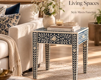 Peut inclure: Une table d'appoint carrée présentant un motif floral incrusté bleu foncé et blanc sur sa surface et ses quatre pieds droits. La table est surmontée d'un vase crème rempli de fleurs blanches, d'une bougie en verre et d'un livre intitulé The Kinfolk Home.