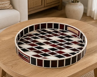 Peut inclure: Un plateau de service rond présentant un motif géométrique en losanges de type arlequin, alternant des tons rouge foncé, noir et blanc. Le plateau possède un rebord surélevé avec un motif en grille assorti et deux poignées découpées intégrées.