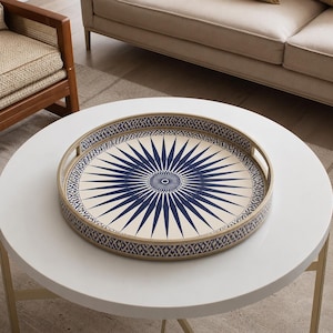May include: A round serving tray with a gold-toned metal rim and integrated handles. The interior base features a cream-colored background with a dark blue sunburst pattern radiating from the center, surrounded by a geometric blue and white border.