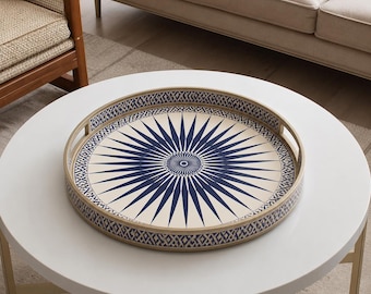 Peut inclure: Un plateau de service rond doté d'un rebord en métal doré et de poignées intégrées. La base intérieure présente un fond crème avec un motif en étoile bleu foncé rayonnant depuis le centre, entouré d'une bordure géométrique bleue et blanche.
