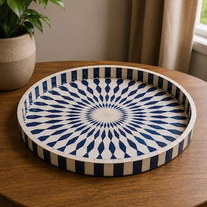 May include: A round tray featuring a radial sunburst pattern in deep blue and off-white. The interior surface displays elongated diamond shapes radiating from the center, while the exterior rim is decorated with a repeating vertical striped pattern.