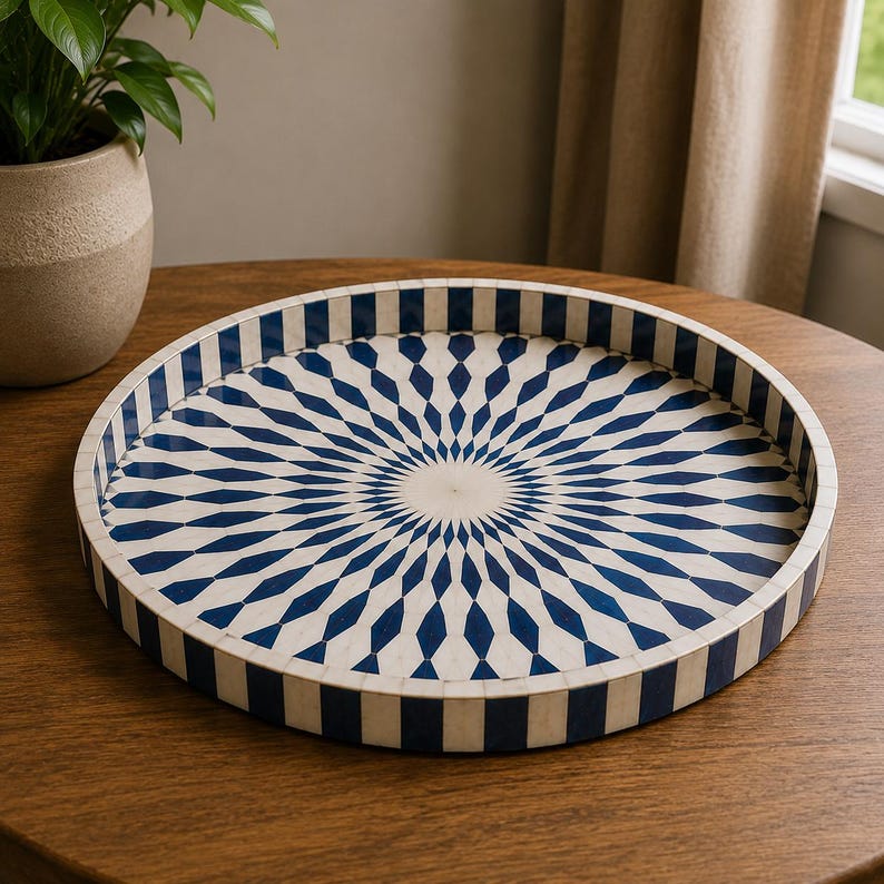 May include: A round tray featuring a radial sunburst pattern in deep blue and off-white. The interior surface displays elongated diamond shapes radiating from the center, while the exterior rim is decorated with a repeating vertical striped pattern.