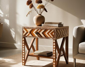 Peut inclure: Une table d'appoint en bois dotée d'un tiroir à motif chevron dans des tons de bois clair et foncé, rehaussé d'incrustations en losanges blancs. La table présente une base en X avec des détails en losanges et une étagère inférieure.