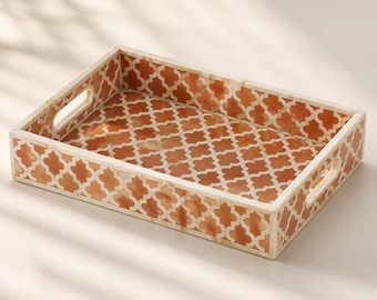 Peut inclure: Un plateau de service rectangulaire orné d'un motif quadrilobé répétitif en orange brûlé et crème. Le plateau présente des bords hauts et deux poignées découpées intégrées sur les côtés courts, avec une finition lisse et polie.