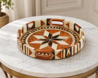 Peut inclure: Un plateau décoratif rond présentant un motif d'étoile géométrique dans des tons terre cuite, crème et noir. Le plateau possède un rebord surélevé avec des poignées intégrées et un motif triangulaire répétitif sur les bords intérieurs et extérieurs.