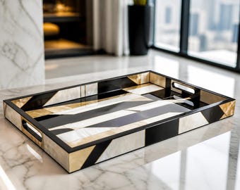 Peut inclure: Un plateau de service rectangulaire présentant un motif géométrique audacieux composé de panneaux alternés noirs et crème. Le plateau possède une finition lisse et polie, un rebord surélevé et des poignées découpées intégrées sur deux côtés.
